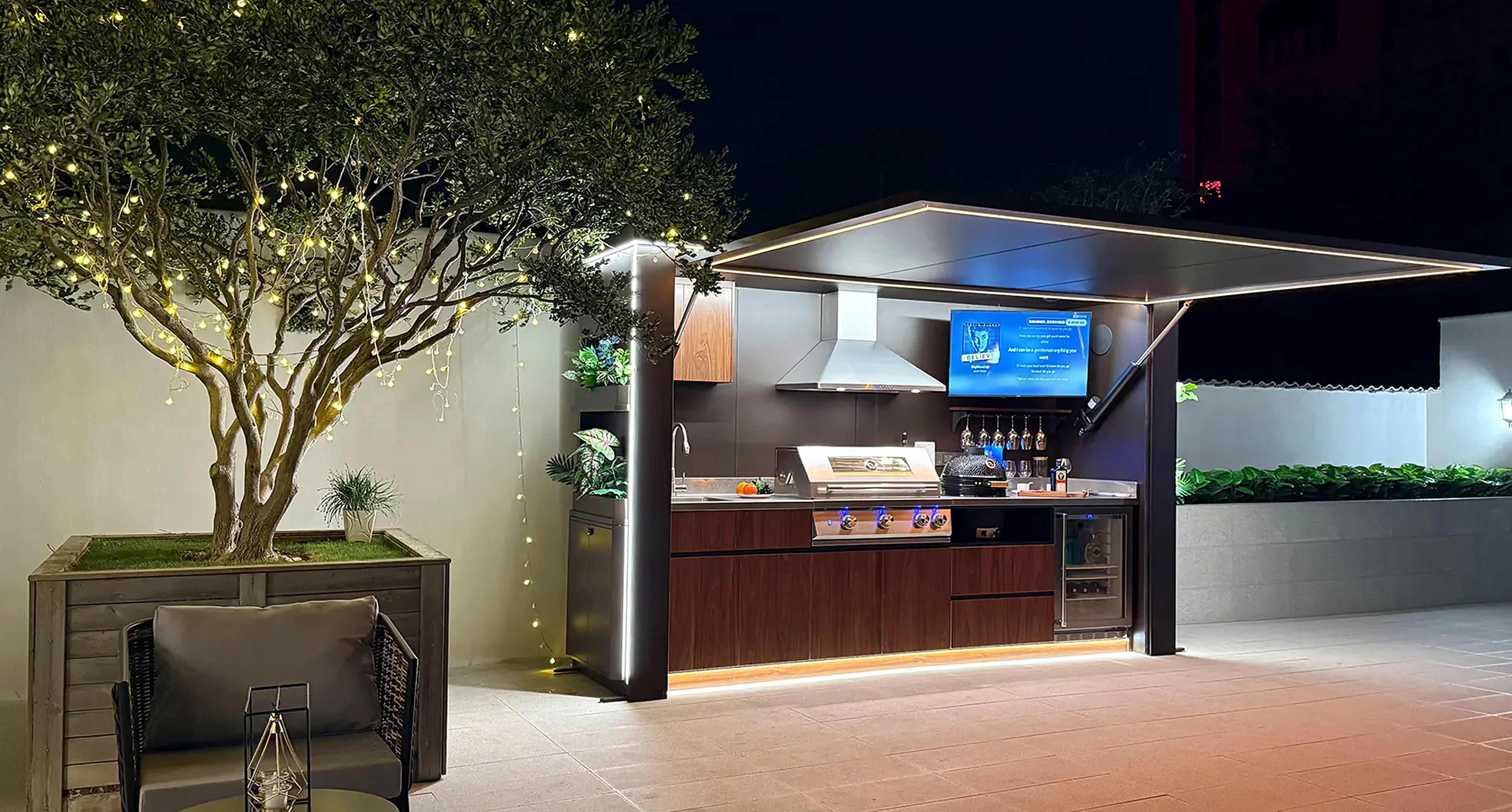 Pod Signature cuisine extérieure de nuit avec éclairage LED, olivier illuminé par des guirlandes et terrasse — photo réelle UHD