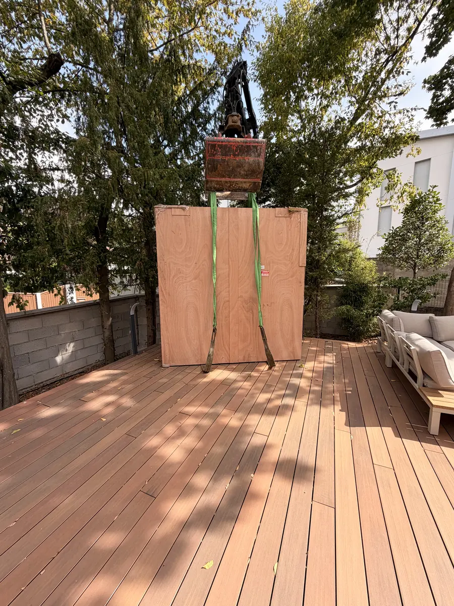 Grutage du Pod BarbecueZone par-dessus le mur du jardin et dépose sur la terrasse en bois existante