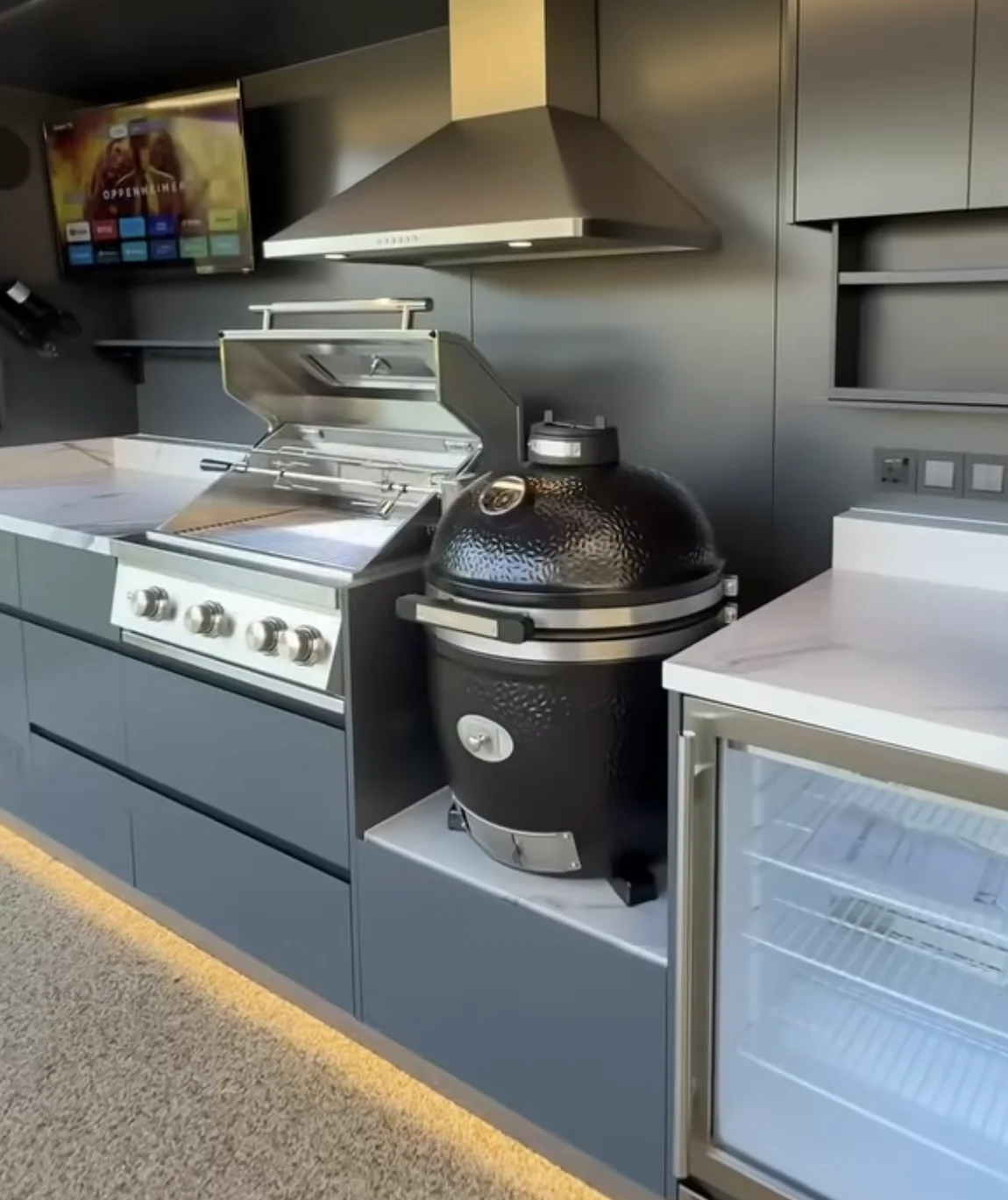 Kamado noir et grill gaz installés côte à côte dans une cuisine extérieure Pod BarbecueZone, sous une même hotte inox, plan de travail continu